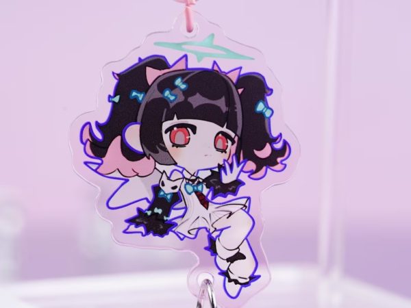 A collection of three holographic acrylic keychains featuring Zenless Zone Zero characters Anby, Nekomata, and Nicole reimagined as magical angels, complete with pink star-shaped clasps and winged heart sub-charms, laid on a pink surface next to a laptop.