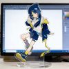 Clear acrylic desktop standees of cute Zenless Zone Zero characters in casual clothing standing on round transparent bases, displayed in front of a computer monitor on a desk.