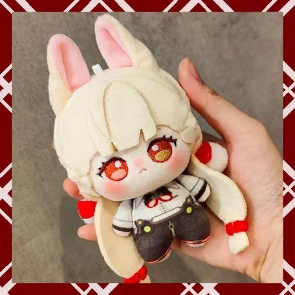 A person holding a 10cm plush cotton doll of the fan-made anime character Alice from Zenless Zone Zero. The chibi doll has blonde hair, fluffy bunny-like ears, large embroidered amber eyes, and wears a white shirt with dark shorts.