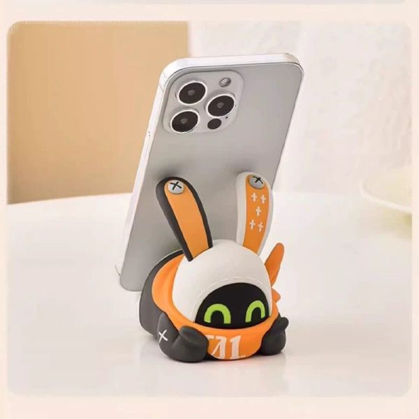 Cute Zenless Zone Zero Eous Bangboo soft silicone figure holding a smartphone horizontally on a white desk.